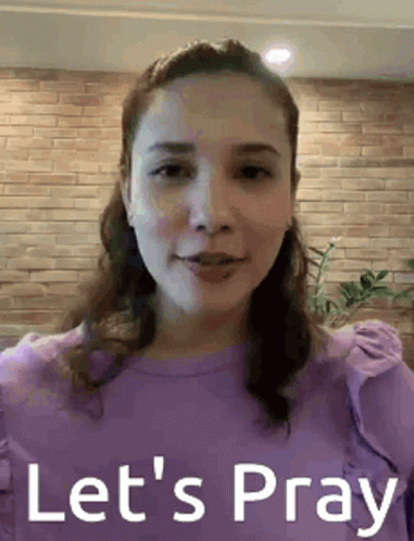 A Woman In A Purple Shirt Is Standing In Front Of A Brick Wall . GIF