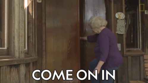 A Woman In A Purple Shirt Is Standing In Front Of A Door That Says Come On In On It GIF
