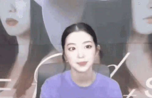 A Woman In A Purple Shirt Is Standing In Front Of A Wall With A Picture Of A Woman . GIF