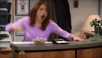 A Woman In A Purple Shirt Is Yawning At A Desk In An Office GIF