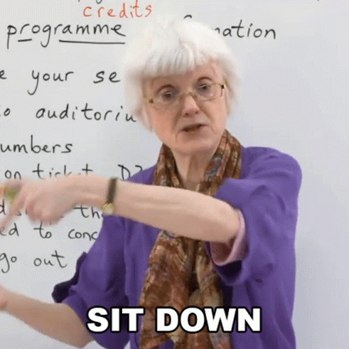 A Woman In A Purple Shirt Says Sit Down In Front Of A Whiteboard GIF