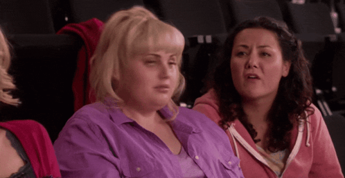 A Woman In A Purple Shirt Sits Next To Another Woman In A Pink Hoodie GIF