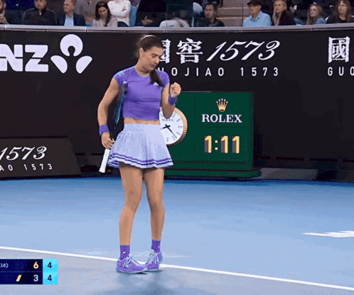 a woman in a purple skirt stands on a tennis court with a rolex sign in the background