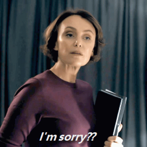 A Woman In A Purple Sweater Is Holding A Book And Says I 'M Sorry GIF