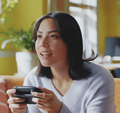 A Woman In A Purple Sweater Is Holding A Video Game Controller In Her Hands GIF