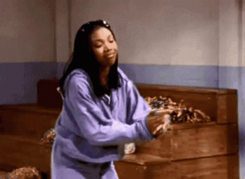 A Woman In A Purple Sweatshirt Is Dancing In Front Of A Wooden Box GIF