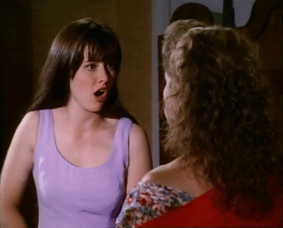 A Woman In A Purple Tank Top Talks To Another Woman In A Red Shirt GIF