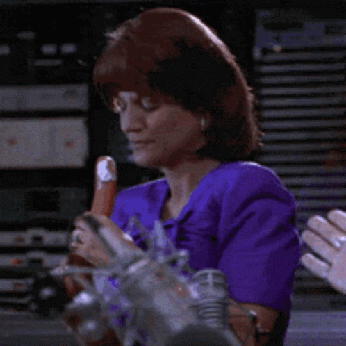 A Woman In A Purple Top Is Holding A Sausage GIF