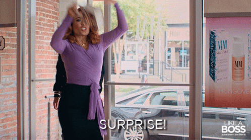 A Woman In A Purple Top Says Surprise In Front Of A Store Window GIF