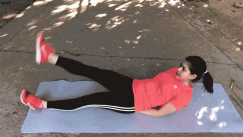 A Woman In A Red Adidas Shirt Is Laying On A Yoga Mat With Her Legs Crossed GIF