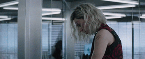 A Woman In A Red And Black Dress Is Standing In A Room With Her Head Down . GIF