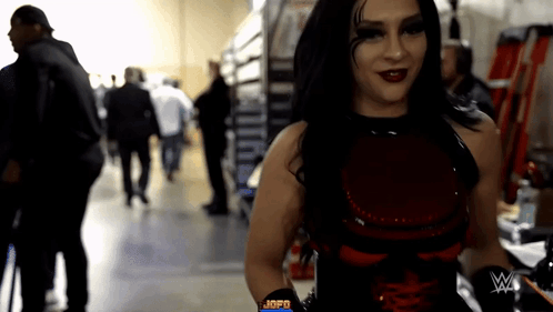 A Woman In A Red And Black Outfit With A W On Her Arm GIF