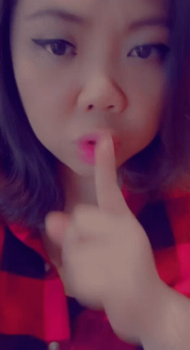 A Woman In A Red And Black Plaid Shirt Holds Her Finger To Her Mouth GIF