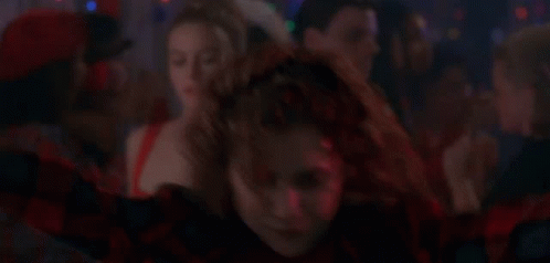 A Woman In A Red And Black Plaid Shirt Is Dancing In Front Of A Crowd . GIF