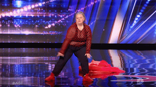 a woman in a red and black plaid shirt is dancing on a stage with a blue background .
