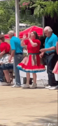 A Woman In A Red And Blue Dress Is Dancing With A Group Of People . GIF