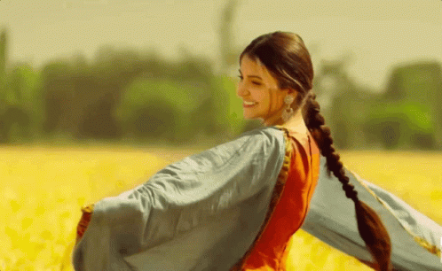 A Woman In A Red And Blue Dress Is Standing In A Field Of Yellow Flowers GIF