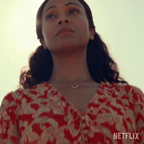 A Woman In A Red And White Floral Top Is Looking Up At The Sky . GIF