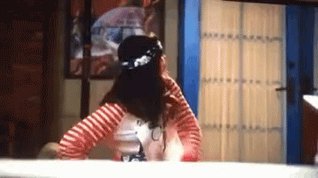 A Woman In A Red And White Striped Shirt Is Standing In Front Of A Blue Door In A Room . GIF