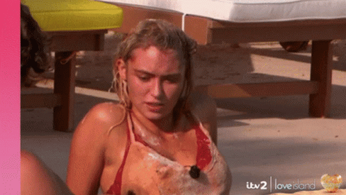 A Woman In A Red Bikini Is Sitting On The Beach With Itv2 Love Island Written On The Bottom GIF