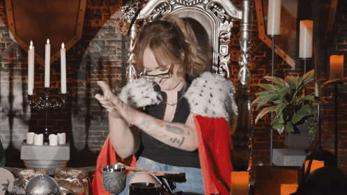 A Woman In A Red Cape Is Sitting In A Chair With Candles In The Background GIF