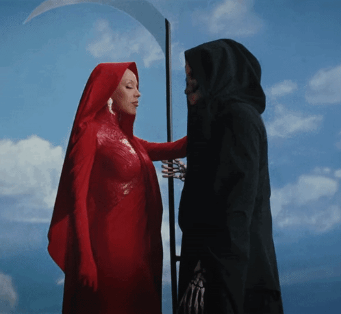 A Woman In A Red Cape Stands Next To A Grim Reaper With A Scythe GIF
