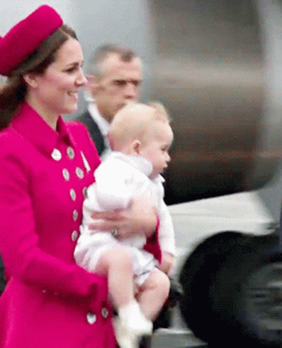 A Woman In A Red Coat Is Holding A Baby In Her Arms GIF