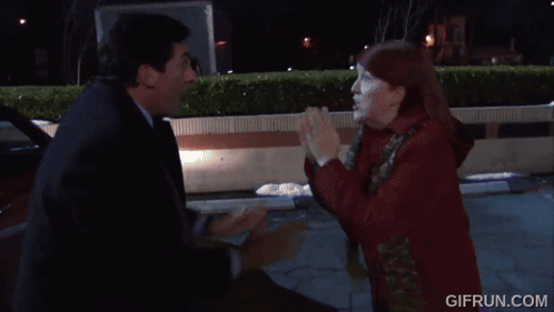 A Woman In A Red Coat Is Standing Next To A Man In A Black Suit . GIF