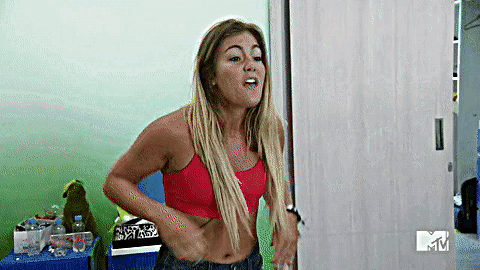 A Woman In A Red Crop Top And Jeans Is Standing In A Room . GIF
