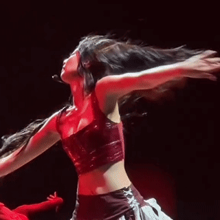 A Woman In A Red Crop Top Is Dancing On A Stage With Her Hair In The Air . GIF
