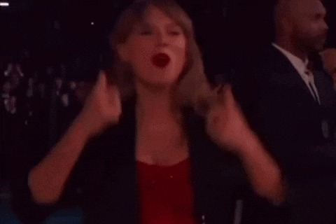 A Woman In A Red Dress And A Black Jacket Is Standing In A Dark Room . GIF
