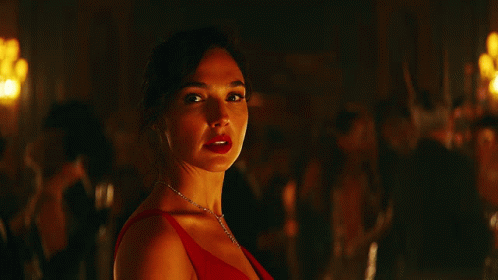 A Woman In A Red Dress And A Diamond Necklace Looks At The Camera GIF