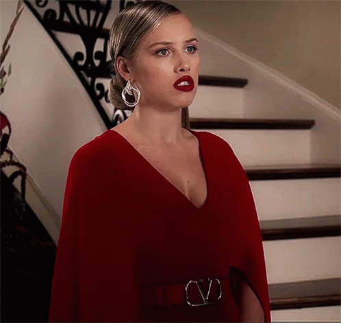 A Woman In A Red Dress And Earrings Is Standing In Front Of Stairs . GIF