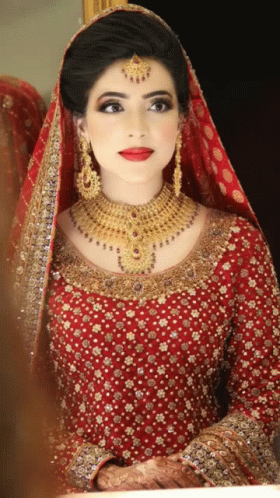 A Woman In A Red Dress And Gold Jewelry Is Looking At Herself In The Mirror GIF
