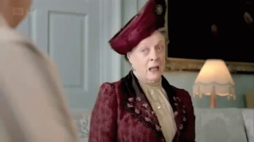 A Woman In A Red Dress And Hat Is Standing Next To A Lamp And Talking To Another Woman . GIF
