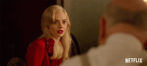 A Woman In A Red Dress And Red Lipstick Is Looking At A Man In A White Shirt . GIF