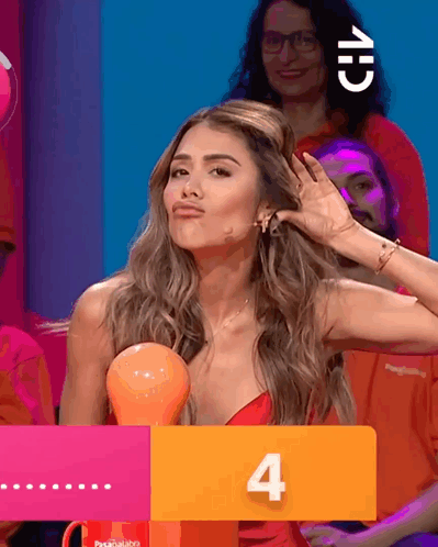 A Woman In A Red Dress Holds Her Hand To Her Ear Behind A Sign That Says 4 GIF