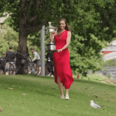A Woman In A Red Dress Is Carrying A Trophy In A Park GIF