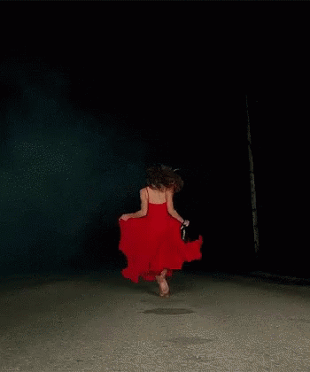 A Woman In A Red Dress Is Dancing Barefoot In The Dark GIF