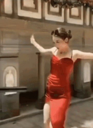 A Woman In A Red Dress Is Dancing On A Sidewalk . GIF