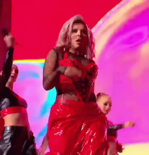 A Woman In A Red Dress Is Dancing On A Stage With A Group Of Dancers . GIF