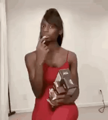 A Woman In A Red Dress Is Holding A Box Of Cereal And A Cigarette In Her Mouth . GIF
