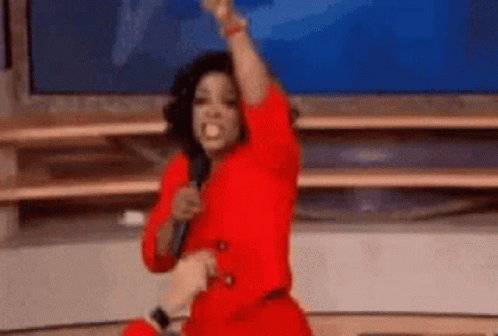 A Woman In A Red Dress Is Holding A Microphone And Raising Her Fist . GIF