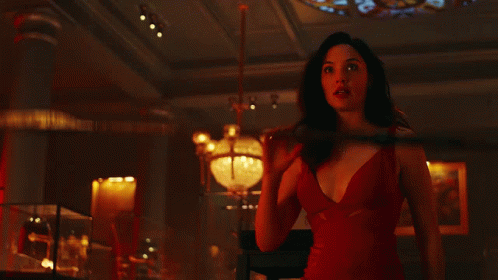 A Woman In A Red Dress Is Holding A Spear In A Dark Room GIF