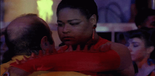 A Woman In A Red Dress Is Hugging A Man With A Bald Head GIF