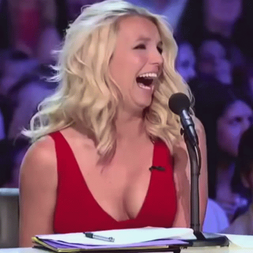 A Woman In A Red Dress Is Laughing While Sitting At A Microphone GIF
