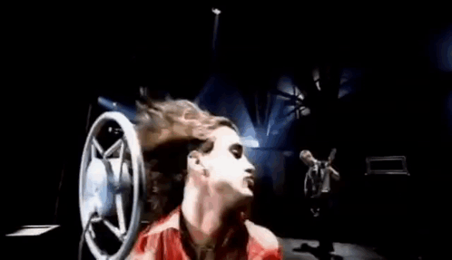A Woman In A Red Dress Is Laying Down With Her Hair Blowing In The Wind In Front Of A Microphone . GIF