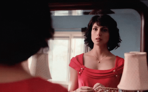 A Woman In A Red Dress Is Looking At Her Reflection In A Mirror GIF