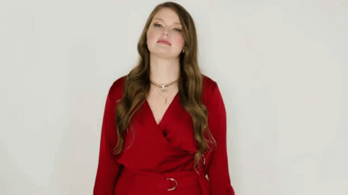 A Woman In A Red Dress Is Making A Funny Face And Giving A Thumbs Up . GIF