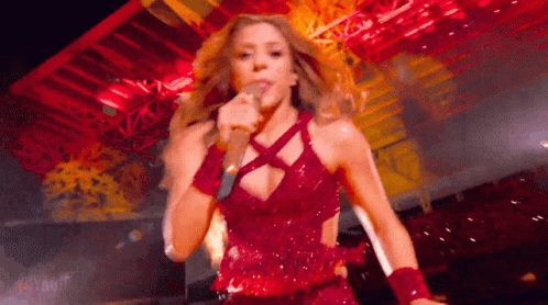 A Woman In A Red Dress Is Singing Into A Microphone . GIF